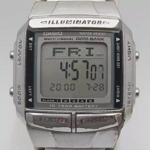 May include: A silver Casio digital watch with a rectangular face. The watch displays the time, date, and day of the week. The watch has multiple buttons for adjusting settings and features the text "ILLUMINATOR" and "WATER RESIST".