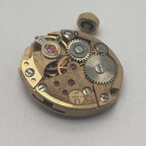 Pode incluir: Um movimento de rel&oacute;gio vintage dourado, com in&uacute;meras pequenas engrenagens, joias e uma haste de corda. O movimento &eacute; marcado com o n&uacute;mero "39" e o s&iacute;mbolo Omega. O design intrincado mostra a precis&atilde;o da relojoaria.