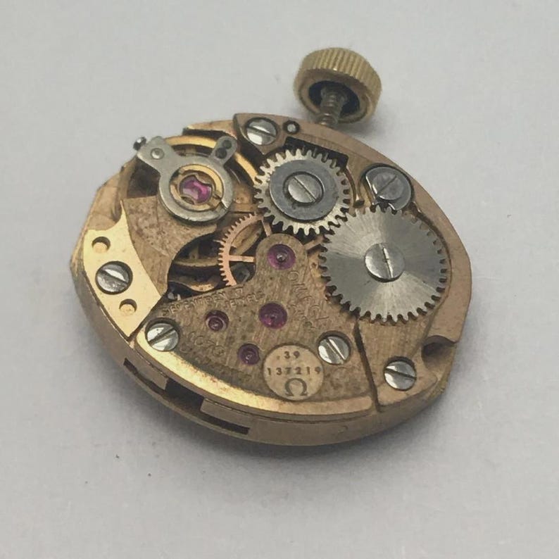 Pode incluir: Um movimento de rel&oacute;gio vintage dourado, com in&uacute;meras pequenas engrenagens, joias e uma haste de corda. O movimento &eacute; marcado com o n&uacute;mero "39" e o s&iacute;mbolo Omega. O design intrincado mostra a precis&atilde;o da relojoaria.