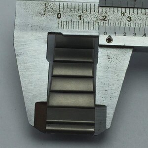 Puede incluir: Primer plano de una correa de reloj met&aacute;lica que se mide con un calibrador plateado. La correa del reloj es una serie de eslabones rectangulares de metal gris. El calibrador muestra medidas en cent&iacute;metros.