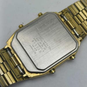 May include: A gold-coloured Citizen watch with a rectangular face and a matching metal strap. The watch's back is visible, displaying text including "CITIZEN WATCH CO." and "WATER RESIST." The strap is made of small, connected links.