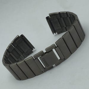 Puede incluir: Una correa de reloj de metal gris oscuro con eslabones rectangulares. La correa est&aacute; desabrochada, mostrando la marca Casio en el cierre. La correa est&aacute; dise&ntilde;ada para un reloj.