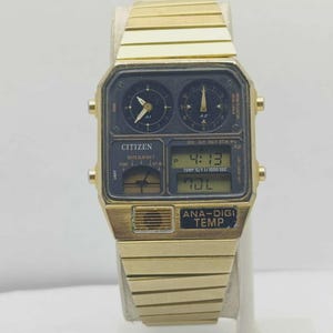May include: A gold-coloured Citizen Ana-Digi Temp watch. The watch has a black face with both analogue and digital displays, showing time, date, and temperature. The watch strap is also gold-coloured.