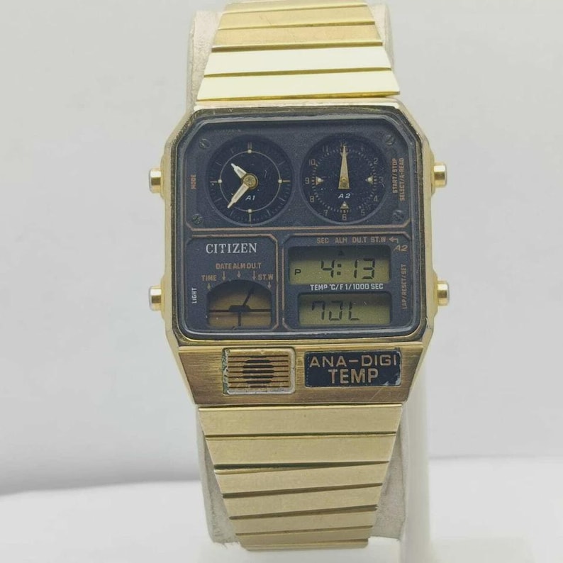May include: A gold-coloured Citizen Ana-Digi Temp watch. The watch has a black face with both analogue and digital displays, showing time, date, and temperature. The watch strap is also gold-coloured.