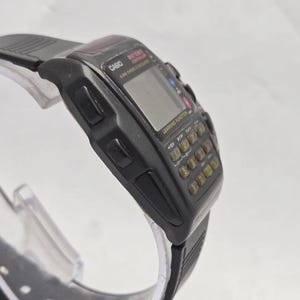 Puede incluir: Un reloj calculadora Casio negro con pantalla digital y teclado completo. El reloj tiene una correa de goma negra y presenta el texto "CASIO" y "LEARNING FUNCTION". El reloj est&aacute; en &aacute;ngulo, mostrando la esfera y el lateral.