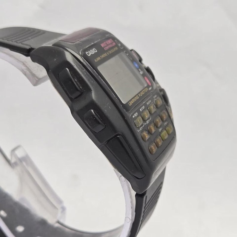 Puede incluir: Un reloj calculadora Casio negro con pantalla digital y teclado completo. El reloj tiene una correa de goma negra y presenta el texto "CASIO" y "LEARNING FUNCTION". El reloj est&aacute; en &aacute;ngulo, mostrando la esfera y el lateral.