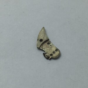 May include: A small, silver-colored watch part with a curved, irregular shape. It features several small holes and intricate detailing, suggesting a mechanical function. The part appears to be made of metal and is likely a component of a vintage or antique timepiece.