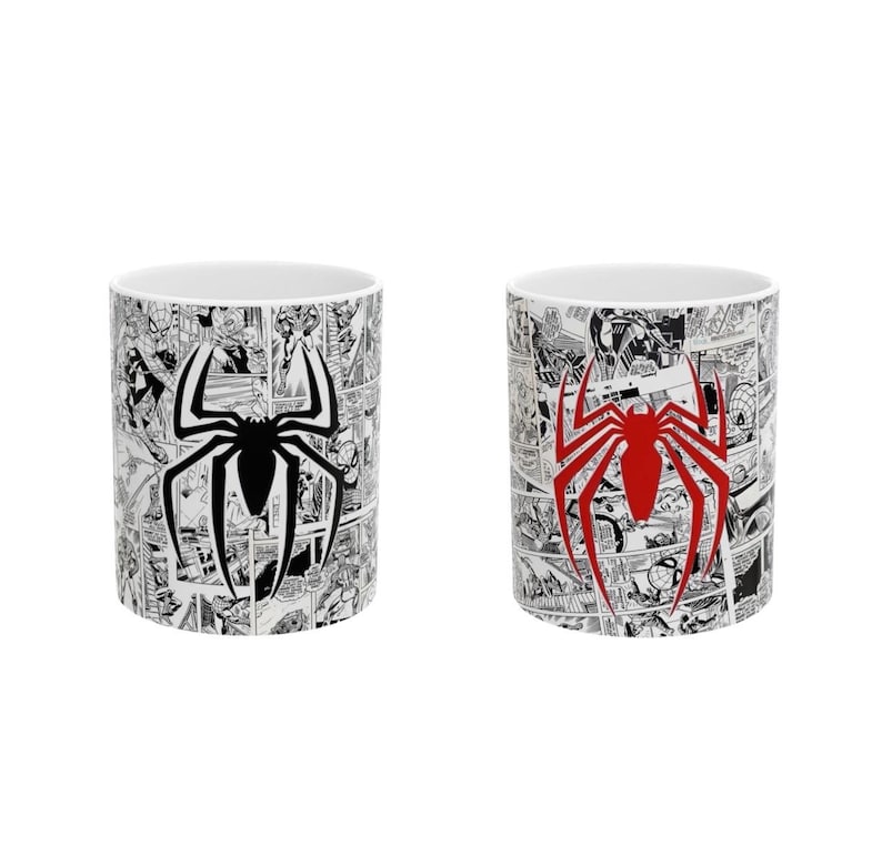 May include: Two white ceramic mugs featuring a comic book design. One mug has a black spider emblem, and the other has a red spider emblem. The mugs are decorated with black and white comic book panels.