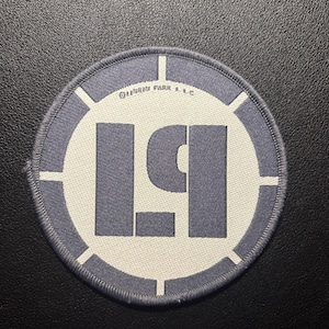 Könnte beinhalten: Runder Aufnäher mit grauem und weißem Design. Der Aufnäher zeigt die stilisierten Buchstaben "LP" in Grau, vor einem weißen Hintergrund. Der äußere Ring ist grau mit weißen Linien. Der Text "LINKIN PARK L.L.C." ist oben aufgedruckt.