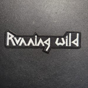May include: Black embroidered patch with the words "Running Wild" in white, stylized lettering. The patch has a unique shape with a black border and is set against a textured black background.