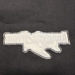 May include: A white embroidered patch with the text "Acoustic Nation" in a stylized font. The patch has a black border and is set against a dark fabric background.