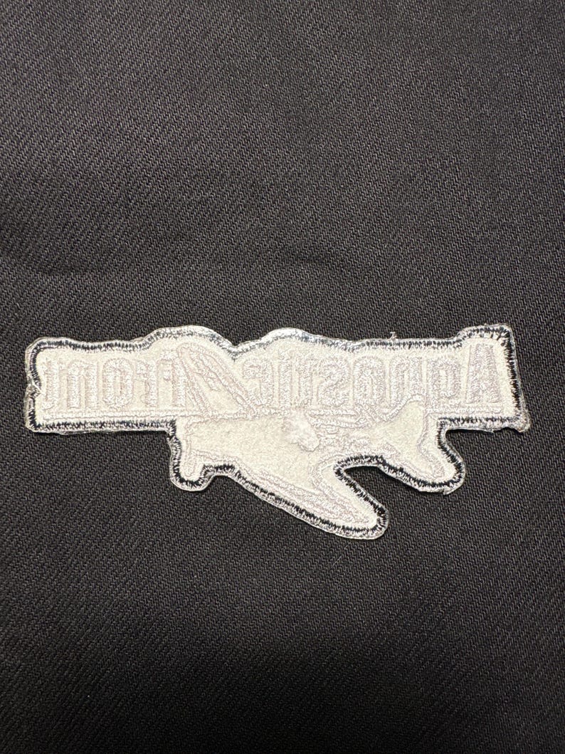 May include: A white embroidered patch with the text "Acoustic Nation" in a stylized font. The patch has a black border and is set against a dark fabric background.