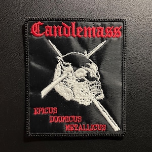 Op de afbeelding: Een rechthoekige zwarte geborduurde patch met de rode tekst Candlemass bovenaan. Daaronder is een witte schedel afgebeeld met twee gekruiste witte zwaarden erachter. De rode tekst Epicus Doomicus Metallicus is onderaan geborduurd.