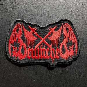 Könnte beinhalten: Ein schwarzer bestickter Aufnäher mit roten Faden-Details. Das Design zeigt zwei gekreuzte Äxte über einem stilisierten roten Schriftzug, der "Deutche" lautet. Flankiert wird der Text von zwei symmetrischen, komplexen roten Drachenflügelmotiven.