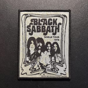 Könnte beinhalten: Ein quadratischer Aufnäher in Schwarz und Weiß mit der Band Black Sabbath. Der Aufnäher zeigt den Namen der Band in einer stilisierten Schrift, die Worte "World Tour 1978" und Bilder der Bandmitglieder. Der Hintergrund ist hellgrau.