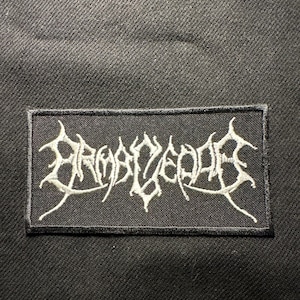 Könnte beinhalten: Schwarzer rechteckiger Aufnäher mit weiß gesticktem Text in einer gotischen Schriftart. Der Aufnäher ist auf einem schwarzen Stoff aufgenäht. Der Aufnäher ist für Kleidung oder Accessoires bestimmt. Der Text ist in einer stilisierten Schriftart.