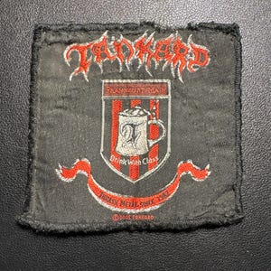 May include: A black patch with red and white text and graphics. The word "Tankard" is at the top in a stylized font. Below is a shield with a beer stein and the text "Drink With Class". The bottom has the text "Thrash Metal Since 1982".