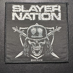 Op de afbeelding: Zwart-wit vierkantige patch met de tekst "SLAYER NATION". Daaronder een schedel met helm en gekruiste zwaarden. De patch heeft een zwarte rand en het copyright luidt "©2020 SLAYER".