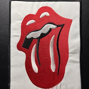 Könnte beinhalten: Gestickter Aufnäher mit dem berühmten roten Lippen- und Zungen-Logo. Das Design befindet sich auf einem weißen Hintergrund mit einem schwarzen Rand. Der Aufnäher ist rechteckig und für das Aufnähen auf Kleidung oder Accessoires gedacht.