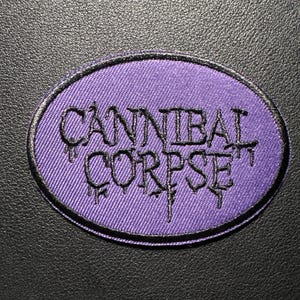 Może przedstawiać: Okrągła naszywka z napisem "CANNIBAL CORPSE" w czarnym, gotyckim kroju pisma na fioletowym tle. Naszywka ma czarną obwódkę i jest umieszczona na czarnej, teksturowanej powierzchni.
