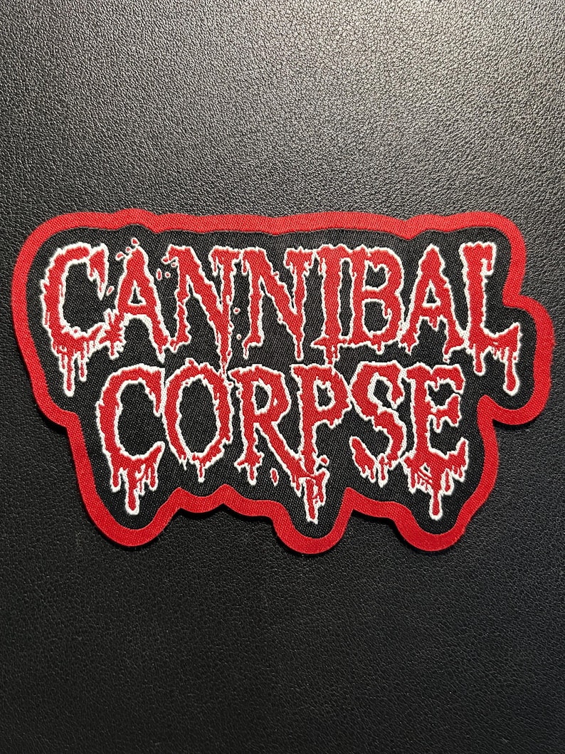 Puede incluir: Un parche bordado rectangular con fondo negro y borde rojo. El texto CANNIBAL CORPSE est&aacute; escrito en una fuente blanca estilizada con un contorno rojo, presentando un efecto l&iacute;quido que gotea que imita el derretimiento o la sangre.