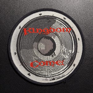 Könnte beinhalten: Runder Aufnäher mit einem Lautsprecherdesign in Grau- und Silbertönen, mit den Worten "Kingdom Come" in Rot. Der Aufnäher hat einen schwarzen Rand und ist vor einem schwarzen Hintergrund platziert.