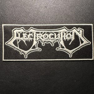 Op de afbeelding: Een rechthoekige zwarte patch met witte geborduurde tekst die "ELECTROCUTION" leest in een gestileerd, gotisch lettertype. De patch heeft een witte rand. Geschikt voor kleding of accessoires.