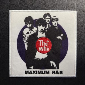 May include: A square embroidered patch featuring a black and white graphic of the band The Who against a purple circular background. A red circular emblem in the center displays the text The Who with an arrow, and the text MAXIMUM R&B is below.