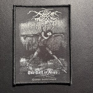 May include: Black and white embroidered patch featuring a stylized illustration of a figure with outstretched arms. The patch has the text "The Cult is Alive" and a band logo at the top. The patch is rectangular with a black border.
