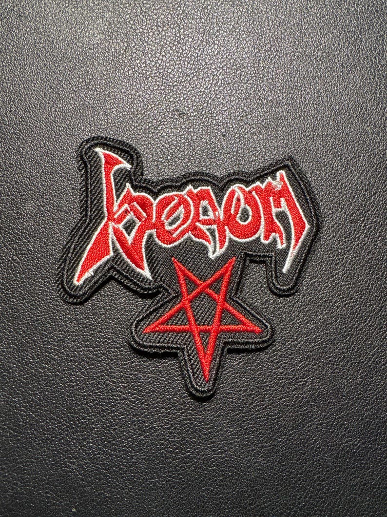 Op de afbeelding: Een zwart embleem met het woord "Venom" in rode, gestileerde letters. Daaronder een rode pentagram. De patch heeft een zwarte rand met witte stiksels.