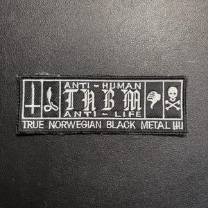 Può includere: Toppa rettangolare in bianco e nero con la scritta "ANTI - HUMAN" e "ANTI - LIFE". La toppa include anche la scritta "TRUE NORWEGIAN BLACK METAL III" e vari simboli, tra cui un teschio e ossa incrociate.