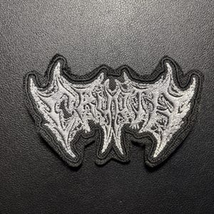 May include: A black and white embroidered patch featuring the word CRYPT in a stylised, jagged, and symmetrical death metal font. The design has a thick black border and intricate white thread detailing that creates a sharp, pointed, and angular appearance.