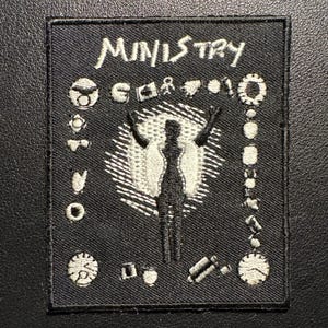 May include: Black square patch with the word "MINISTRY" in white, stylized lettering. The patch features a central figure with raised arms, surrounded by various white symbols. The patch is likely for a band or music group.