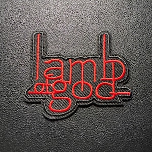 Könnte beinhalten: Ein schwarzer, gestickter Aufnäher mit den Worten "Lamb of God" in roter, stilisierter Schrift. Der Aufnäher hat einen schwarzen Rand und ist auf einem strukturierten schwarzen Hintergrund platziert.