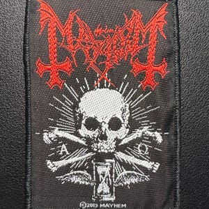 Könnte beinhalten: Schwarzer quadratischer Aufnäher mit rotem und weißem Stickdesign. Mit einem Totenkopf mit gekreuzten Knochen, einer Sanduhr und dem Wort "Mayhem" in einer stilisierten Schriftart. Der Text "©2019 MAYHEM" ist ebenfalls vorhanden.