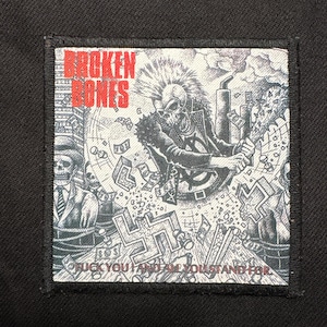 May include: A square patch with a black border. The black and white illustration features a skull with a mohawk, holding a spiked club, with the words "BROKEN BONES" in red. The text "FUCK YOU AND AM YOU STAND FOR" is also present.