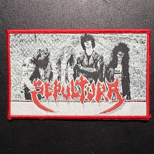 Könnte beinhalten: Ein rechteckiger Aufnäher mit rotem Rand zeigt ein Schwarz-Weiß-Bild einer Band. Der Name der Band, "SEPULTURA", ist in roter, stilisierter Schrift am unteren Rand dargestellt. Der Hintergrund ist ein strukturiertes Graustufenbild.