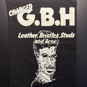Könnte beinhalten: Ein rechteckiger schwarzer Stoffaufnäher mit weißem Siebdrucktext, der CHARGED G.B.H und Leather, Bristles, Studs and Acne lautet. Unter dem Text befindet sich eine weiße grafische Illustration einer Person mit einer stacheligen Frisur.