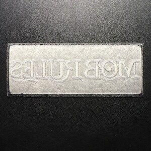 May include: A rectangular patch with the word "MOB RULES" embroidered in white thread. The patch has a black border and is set against a black background. The text is in a stylized font.