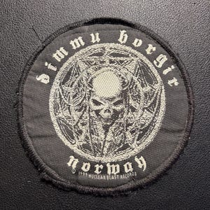 Puede incluir: Parche circular negro con texto blanco y un diseño central. El texto dice "Dimmu Borgir" y "Norway". El diseño central presenta una calavera y patrones en forma de estrella. Este parche es un artículo relacionado con la música.