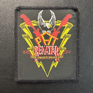 Op de afbeelding: Zwart vierkantige patch met de tekst "PAT BENATAR WIDE AWAKE IN DREAMLAND". Het ontwerp bevat rode gitaren, gele bliksemschichten en een witte adelaar. De patch heeft een zwarte rand.