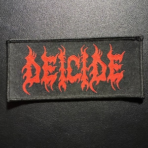 May include: A rectangular black patch with the word "DEICIDE" embroidered in bright red, stylized, flame-like lettering. The patch is likely for clothing or accessories.
