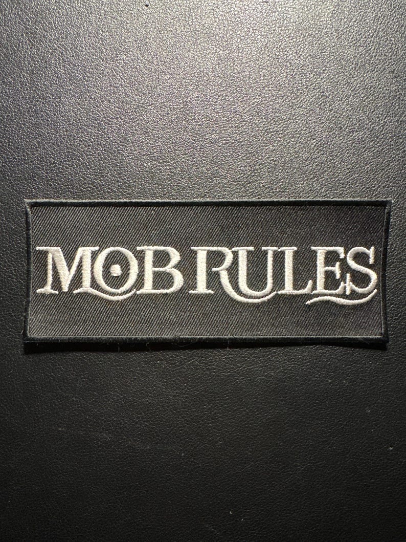 May include: A rectangular black patch with the words "MOB RULES" embroidered in white. The text is in a stylized font. The patch is likely for clothing or accessories.