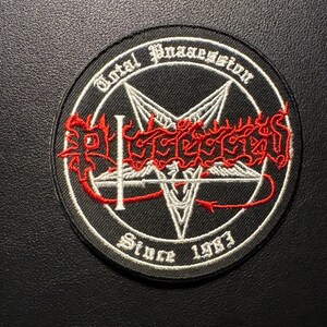 May include: Round black patch with white and red embroidered design. The patch features a pentagram, the text "Total Possession" and "Since 1983". The text and design are in white and red.