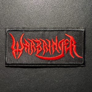 Könnte beinhalten: Ein rechteckiger schwarzer Aufnäher mit dem Wort "WARBRINGER" in roter, stilisierter, gotischer Schrift gestickt. Der Aufnäher, wahrscheinlich für eine Jacke oder Tasche, ist vor einem dunklen, strukturierten Hintergrund platziert.