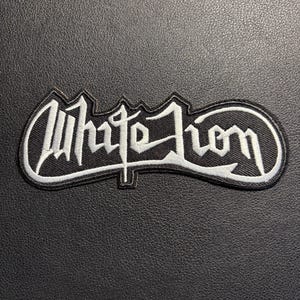 May include: Embroidered patch with the words "White Lion" in white script on a black background. The patch has a white border and is rectangular. The patch is designed for application on clothing or accessories.