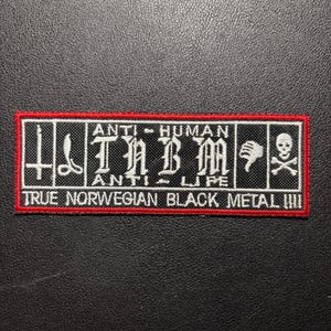 May include: A rectangular embroidered patch with a red border and black background. It features white text reading ANTI-HUMAN, TNBM, ANTI-LIFE, and TRUE NORWEGIAN BLACK METAL. Graphics include an inverted cross, a thumbs-down icon, and a skull and crossbones.