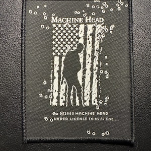 Könnte beinhalten: Schwarzer quadratischer Aufnäher mit dem Text "MACHINE HEAD" über einer weißen Silhouette einer Person vor einer stilisierten amerikanischen Flagge. Der Aufnäher enthält den Text "© 2008 MACHINE HEAD" und "UNDER LICENSE TO HI:FI Ent..."