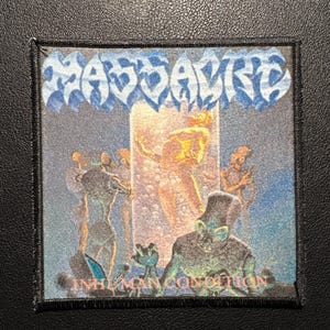 Könnte beinhalten: Quadratischer Aufnäher mit dem Wort "MASSACRE" in blauem, stilisiertem Text oben. Der Aufnäher zeigt eine surreale Illustration mit Figuren und dem Text "INHUMAN CONDITION" in Rosa unten. Der Aufnäher hat einen schwarzen Rand.