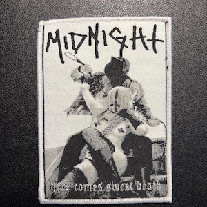 Könnte beinhalten: Ein schwarz-weißer Aufnäher mit dem Wort "MIDNIGHT" in einer kräftigen, stilisierten Schriftart. Der Aufnäher zeigt eine Grafik von zwei Figuren in einem Kampf, mit dem Satz "here comes sweet death" darunter. Der Aufnäher hat einen weißen Rand.